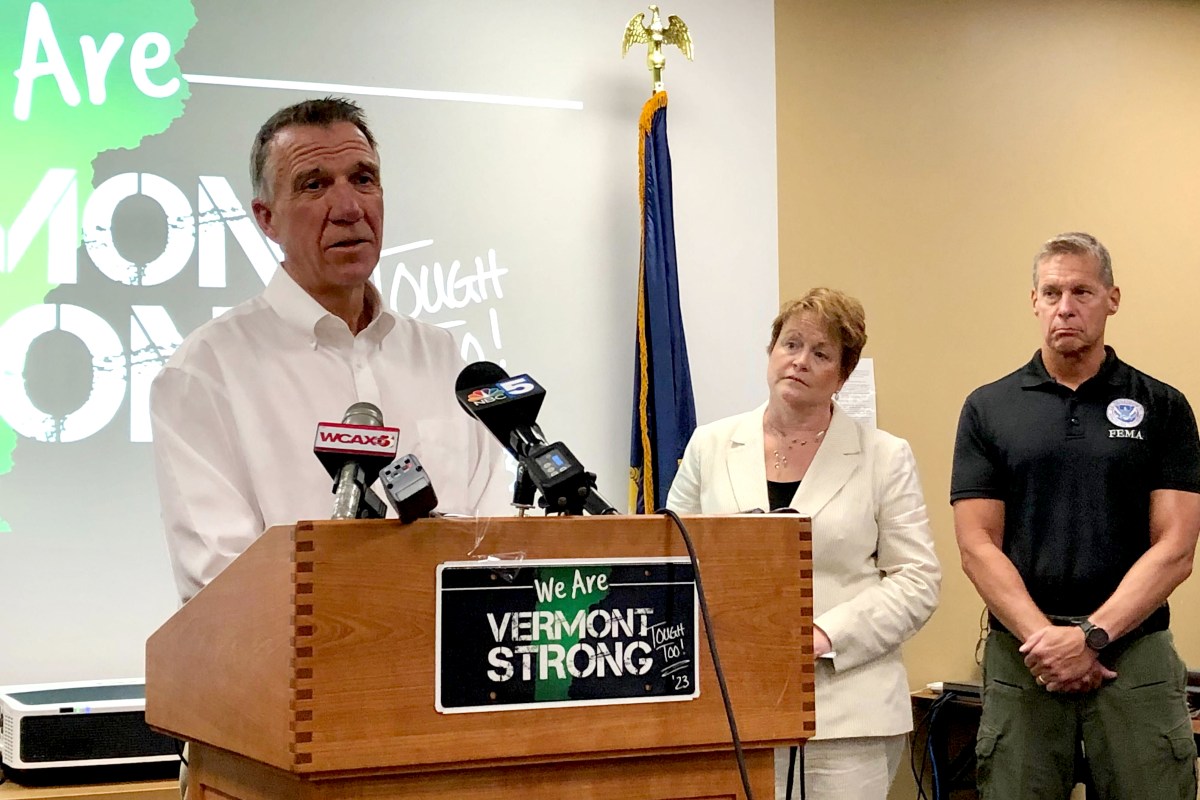 A man in a white shirt stands behind a podium that says "We Are Vermont Strong" on it.