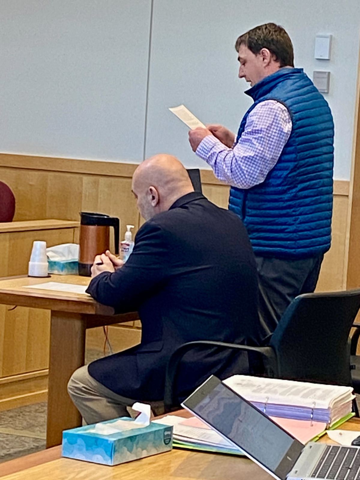 Two men sitting in a courtroom with papers in front of them.