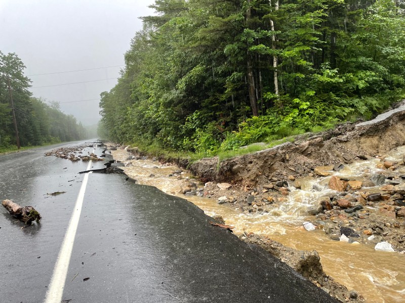 a flooded road with rocks and trees in the background.