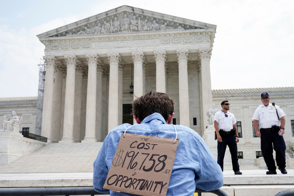 a man holding a sign in front of the supreme court.