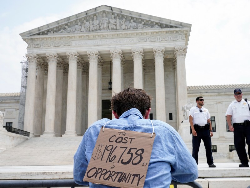 a man holding a sign in front of the supreme court.