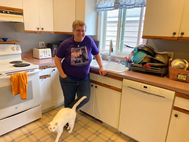 A woman standing in a kitchen with a cat.