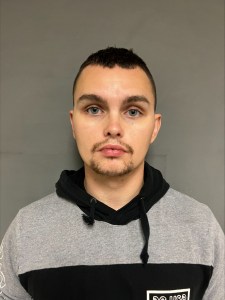 A man in a grey hoodie standing in front of a wall.