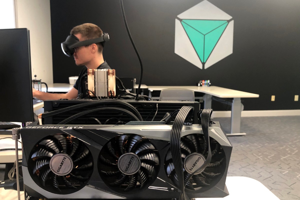 A man is sitting in front of a computer with a gaming rig.