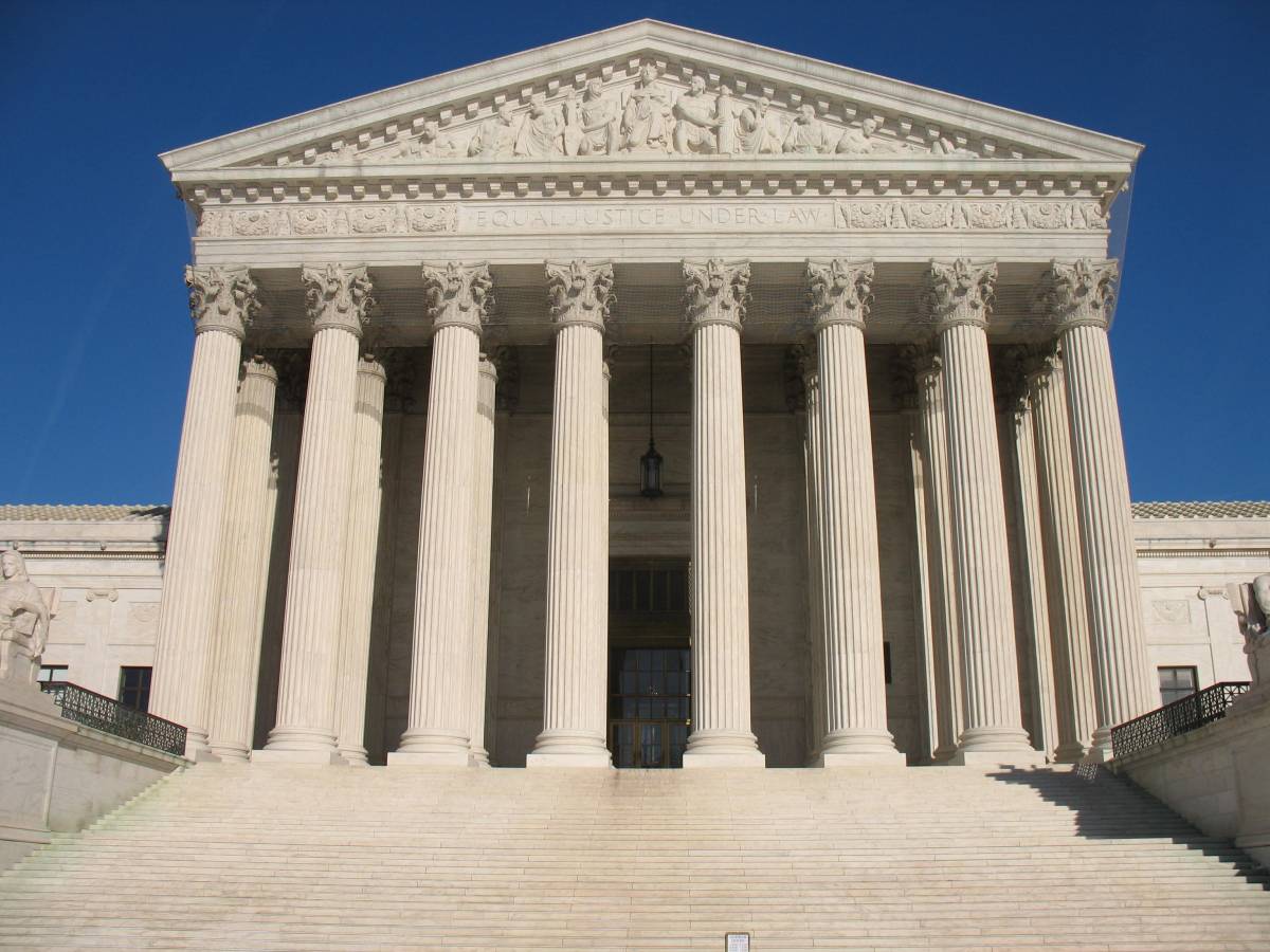 The image shows the front exterior of the United States Supreme Court building, featuring its grand steps and classical columns under a clear blue sky.