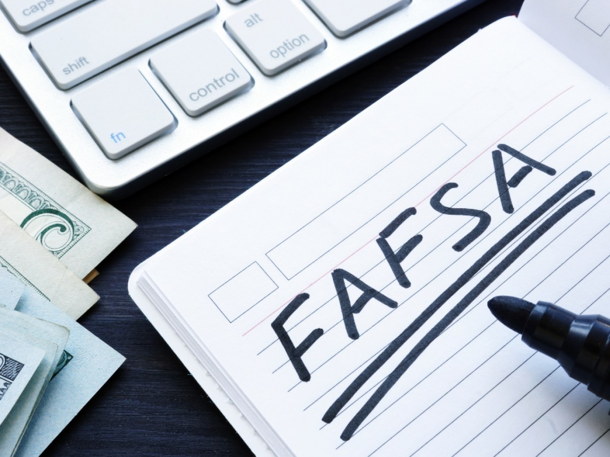 A notebook with the word fafsa written on it next to money and a keyboard.