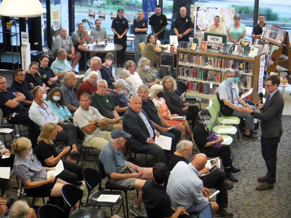 A man speaks to a crowd of people in a library.