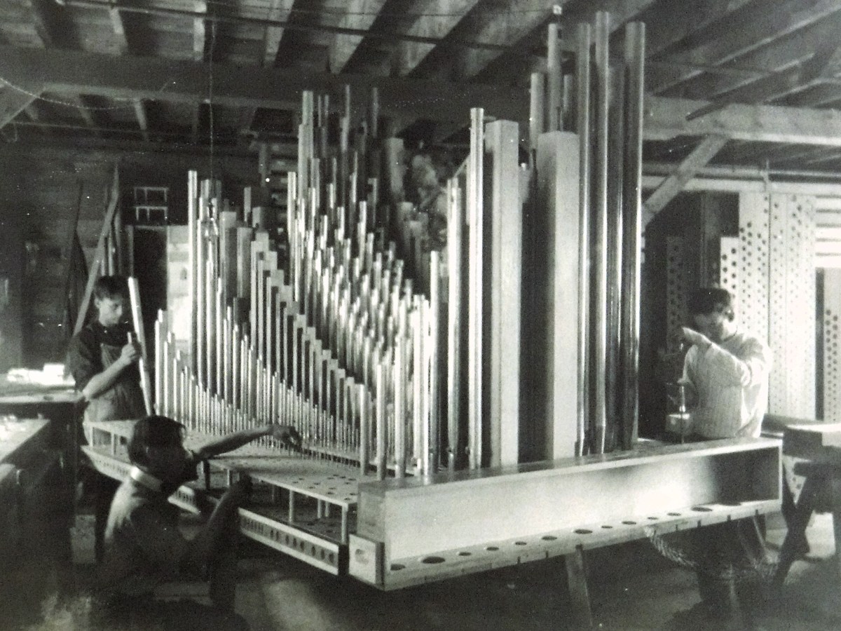 Men working on a pipe organ in a factory.