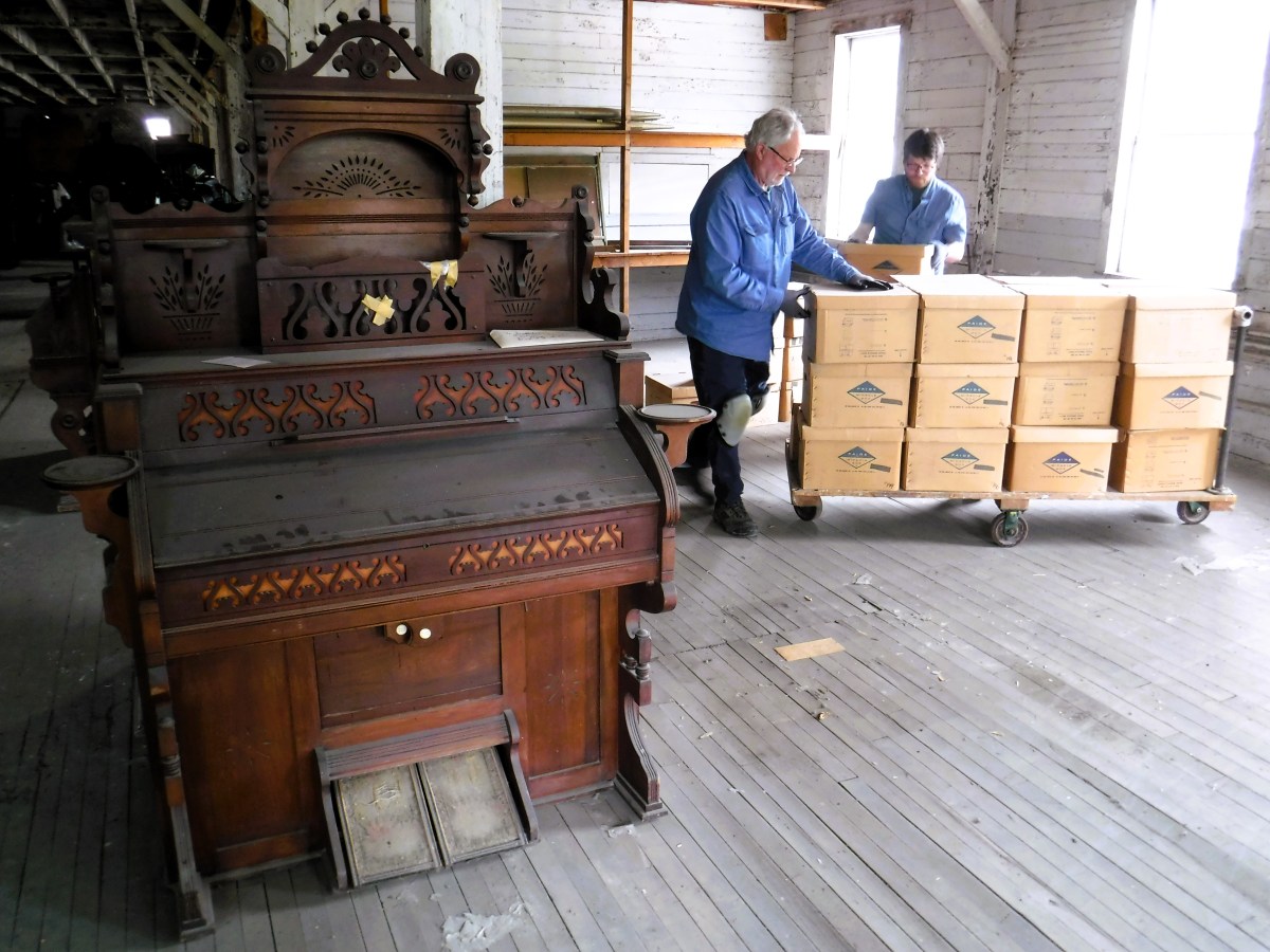 Two men standing next to an old piano in a room.