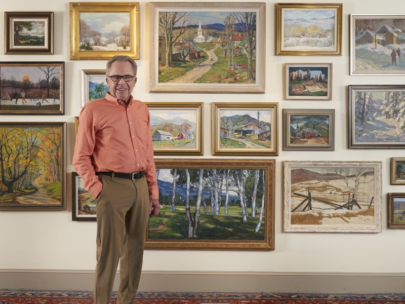 A man standing in front of a wall full of paintings.