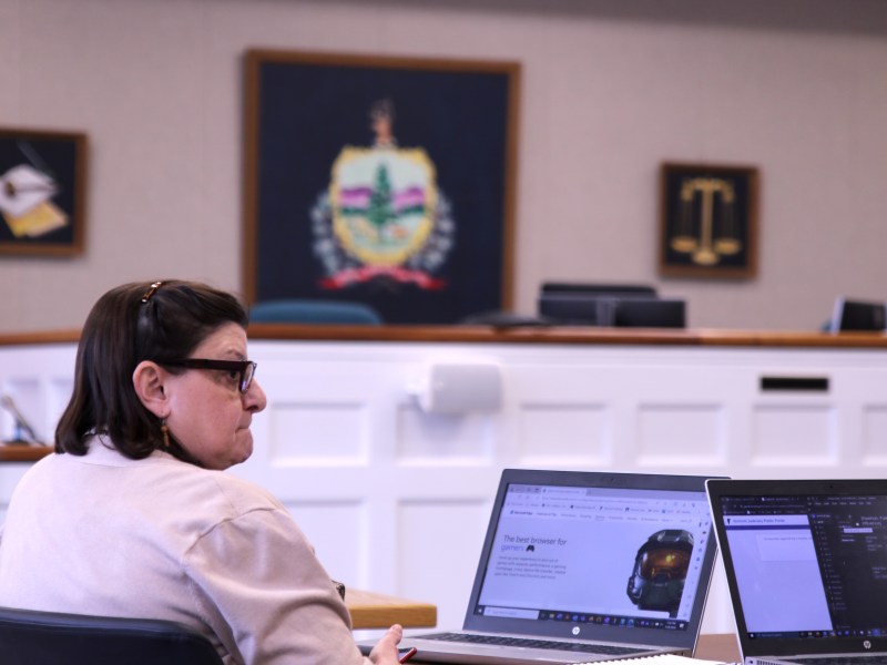 A woman sits in front of a laptop in a courtroom.