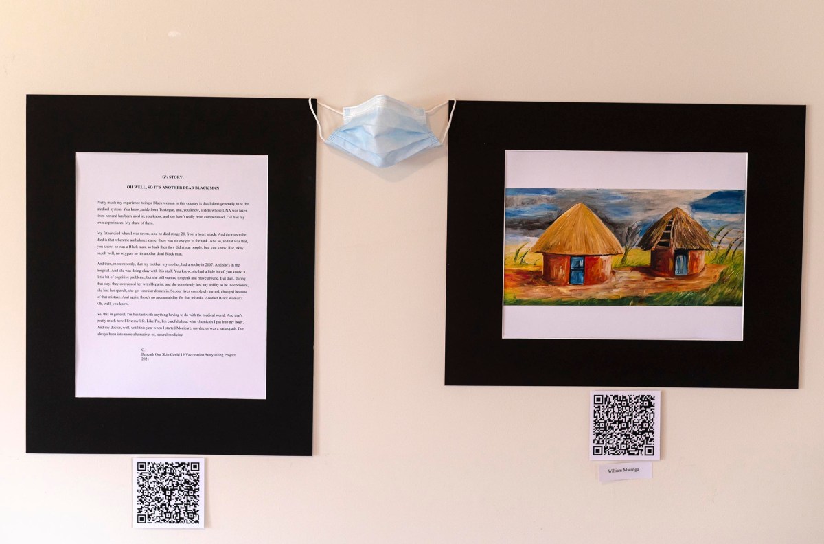 Art exhibition wall featuring two framed paintings of rural huts, a text panel, and a mask hanging between them, with qr codes below each frame.