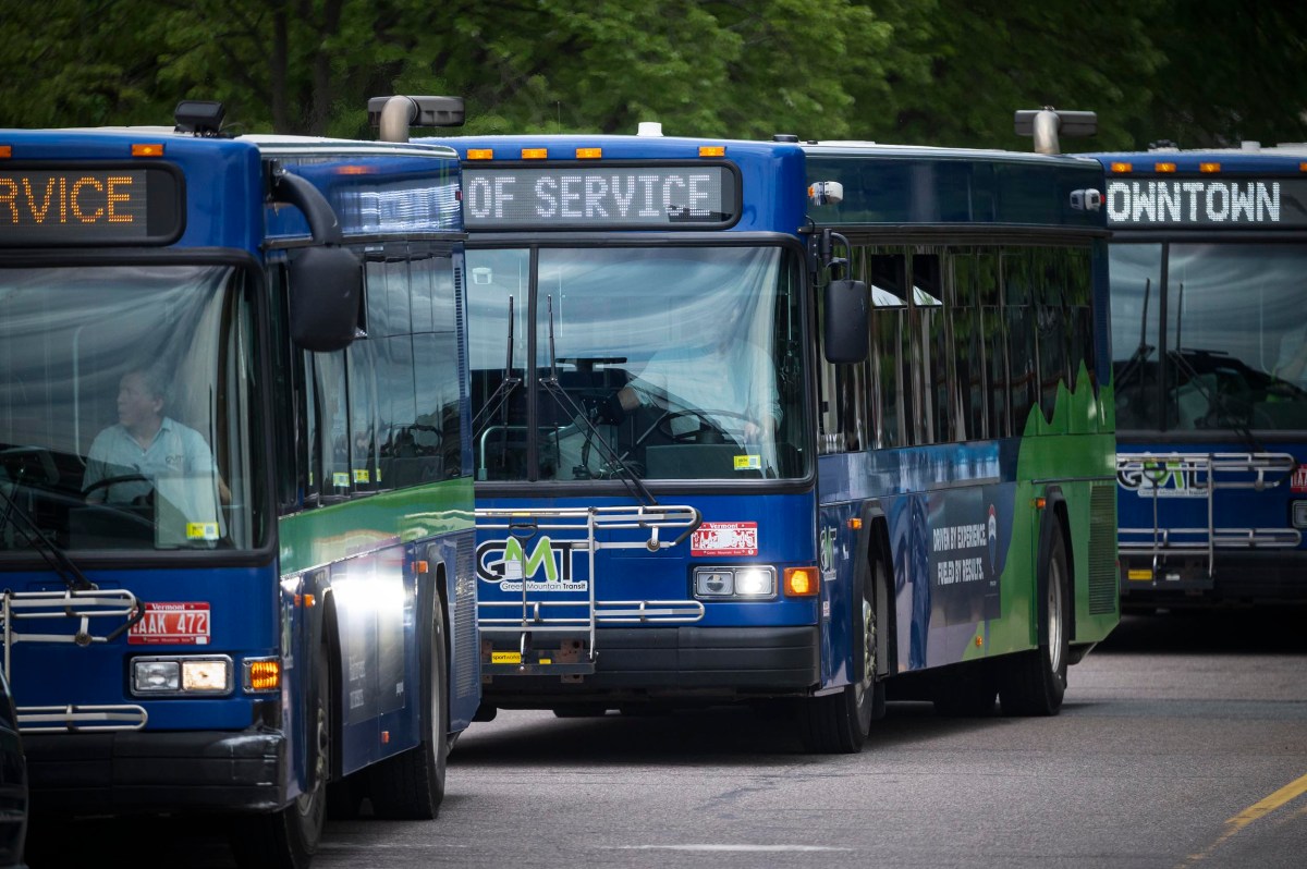 Three city buses are parked on a street. The front bus displays "Out of Service" on its destination sign. Trees are visible in the background.