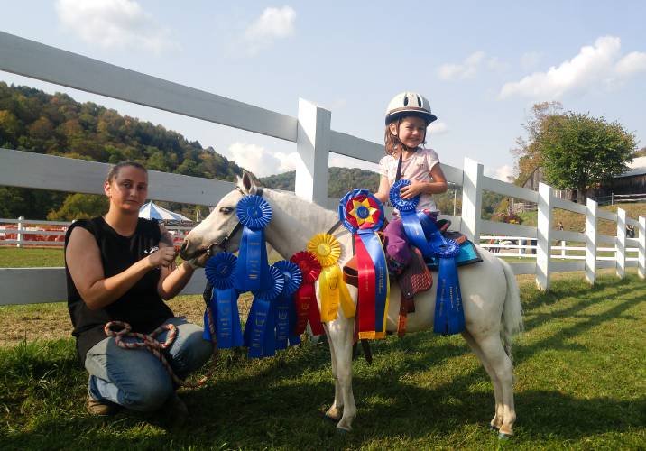 Young equestrian with awarded ribbons on a pony, accompanied by an adult.