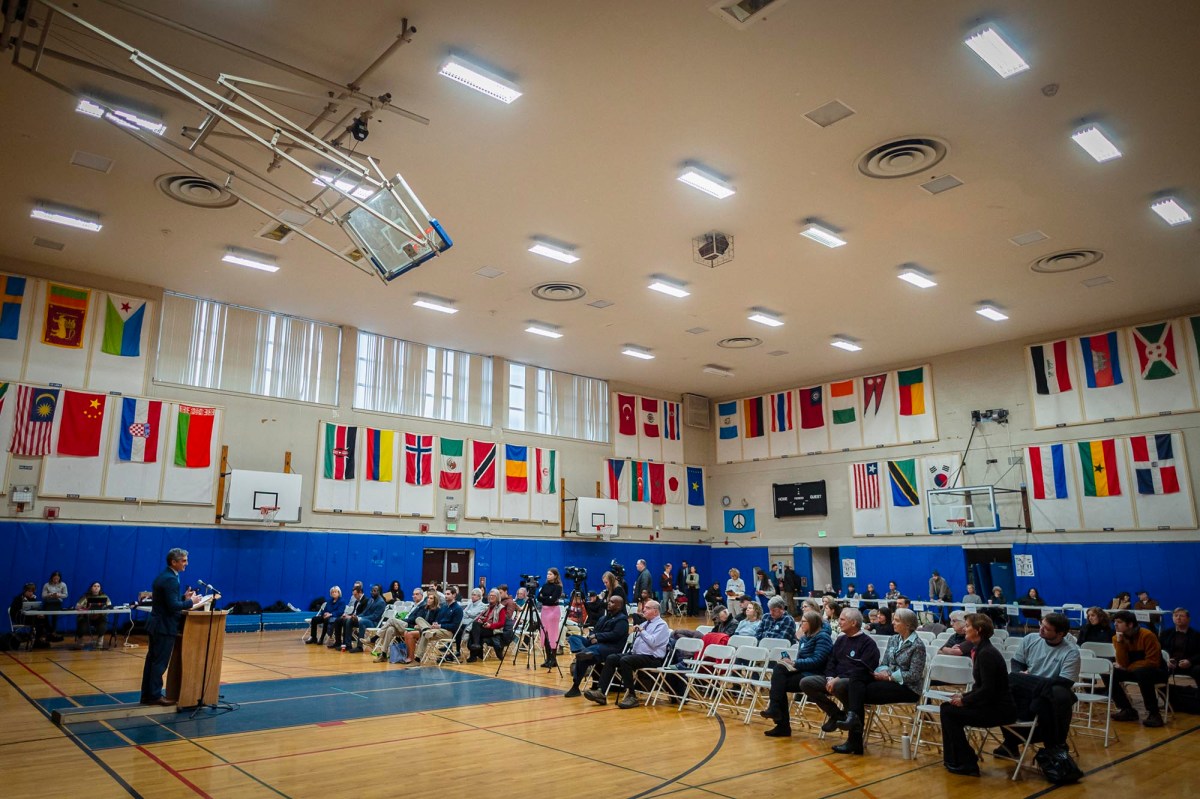 A group of people sitting in a gymnasium with flags in the background.