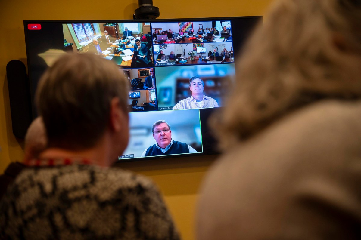 A group of people watching a video conference on a large screen.