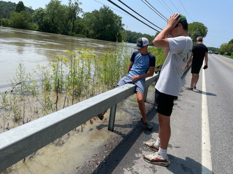 a group of people standing on the side of a flooded road.