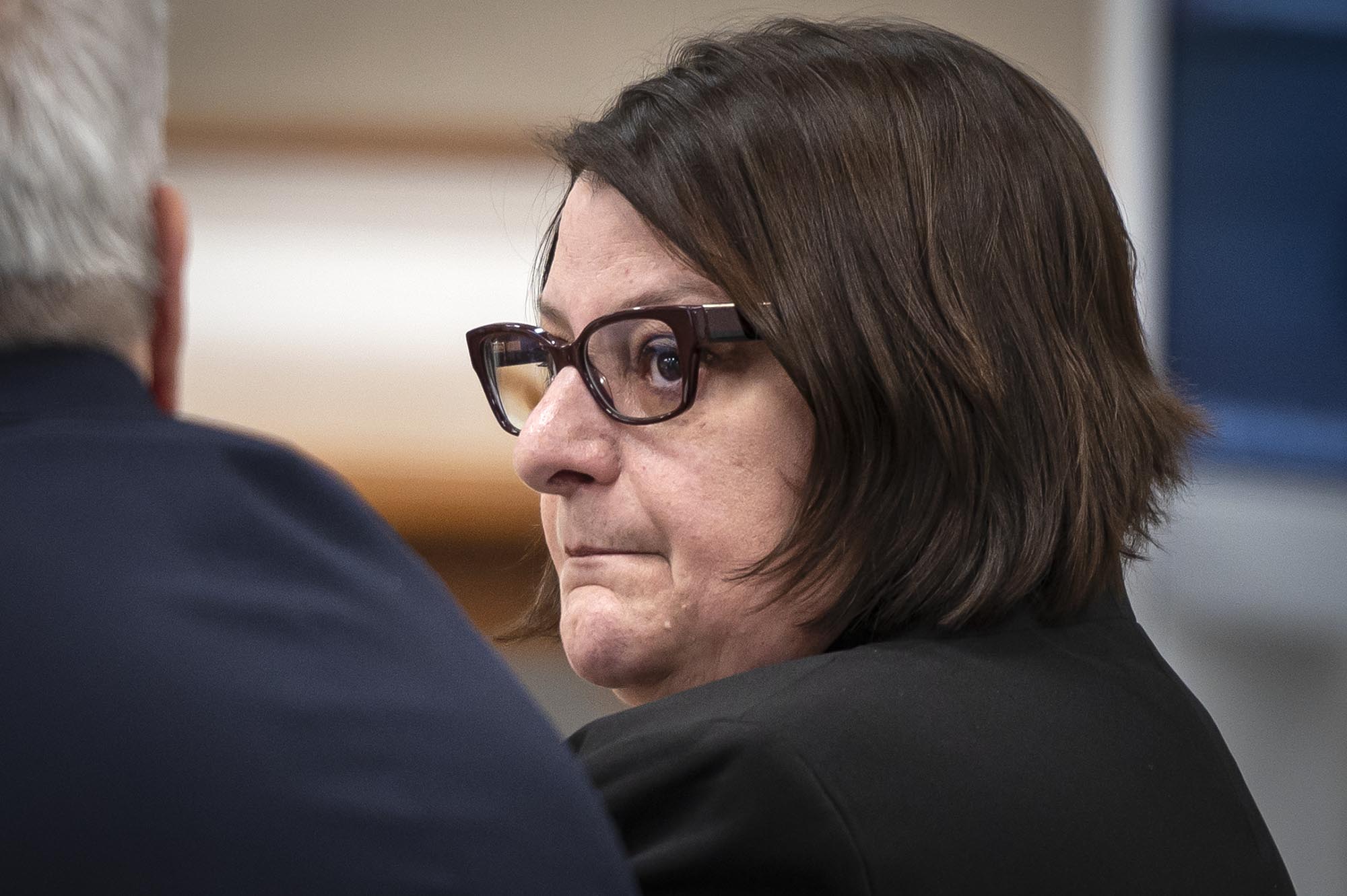 A woman in glasses is sitting in a courtroom.
