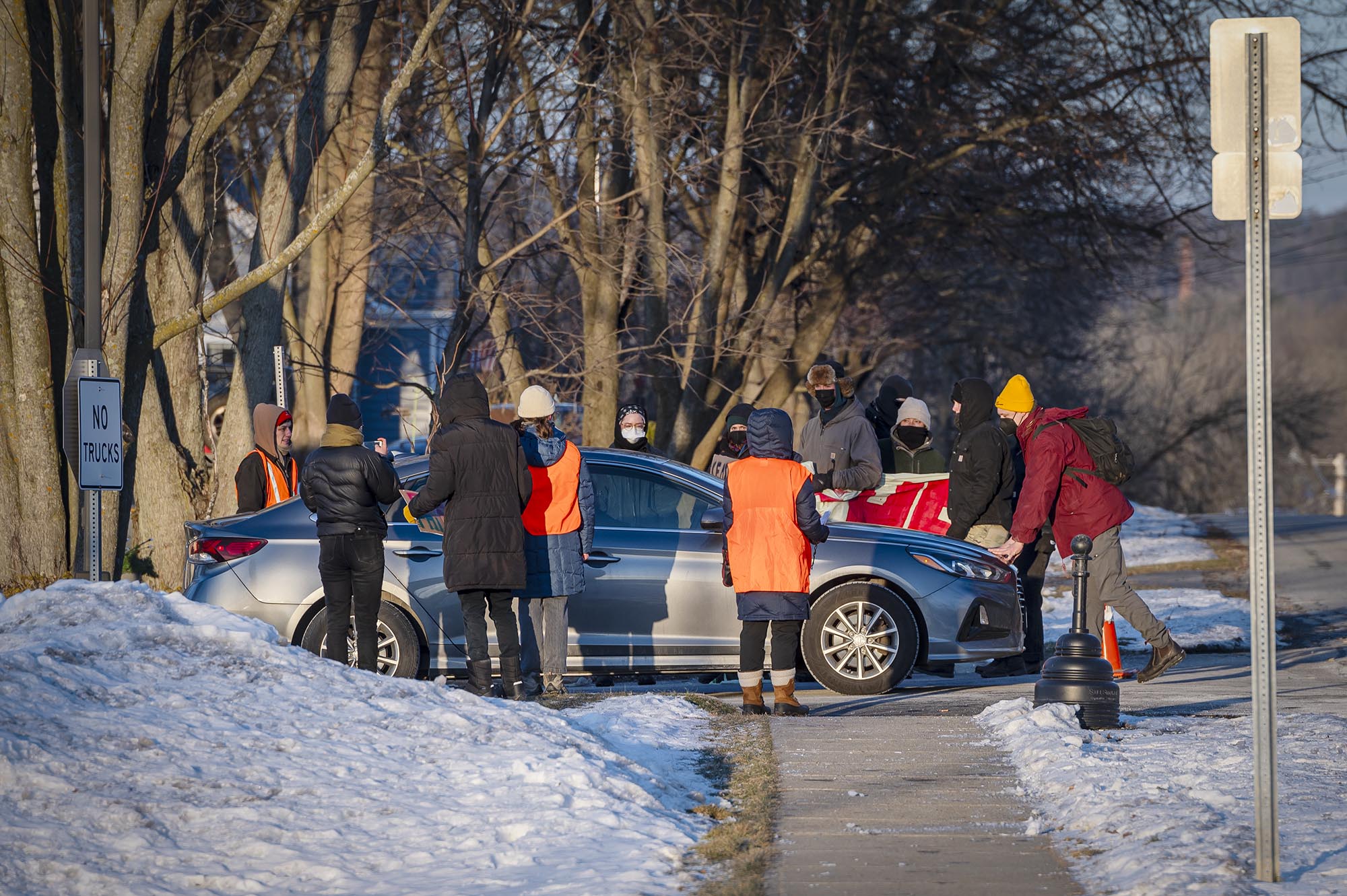 A group of people standing next to a car on a snowy sidewalk.