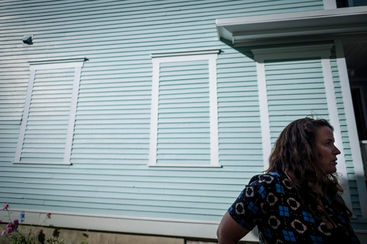 A woman standing in front of a house with shutters.