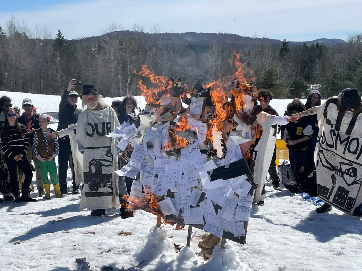 A group of people watching papers burning on a sculpture at an outdoor event with snow on the ground.
