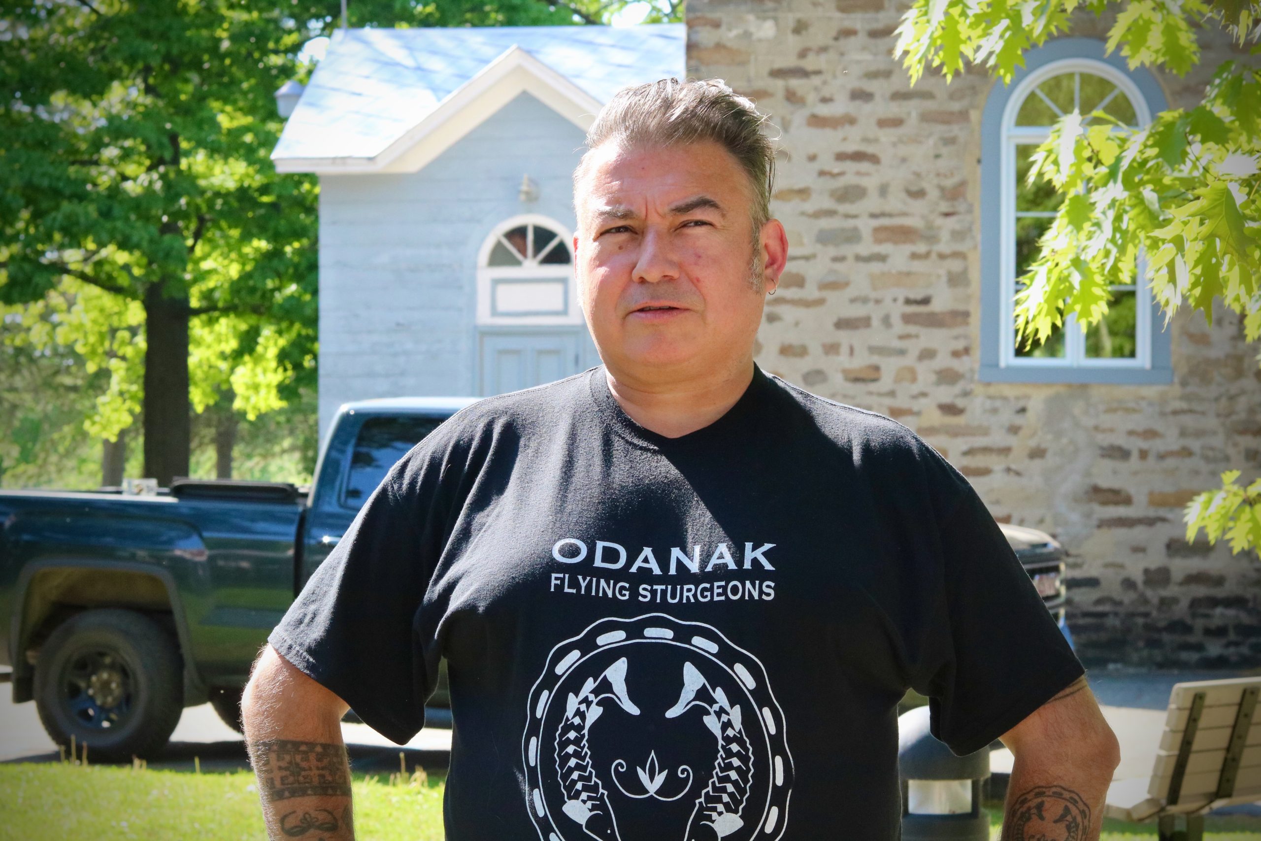 A man wearing a black t - shirt stands in front of a church.
