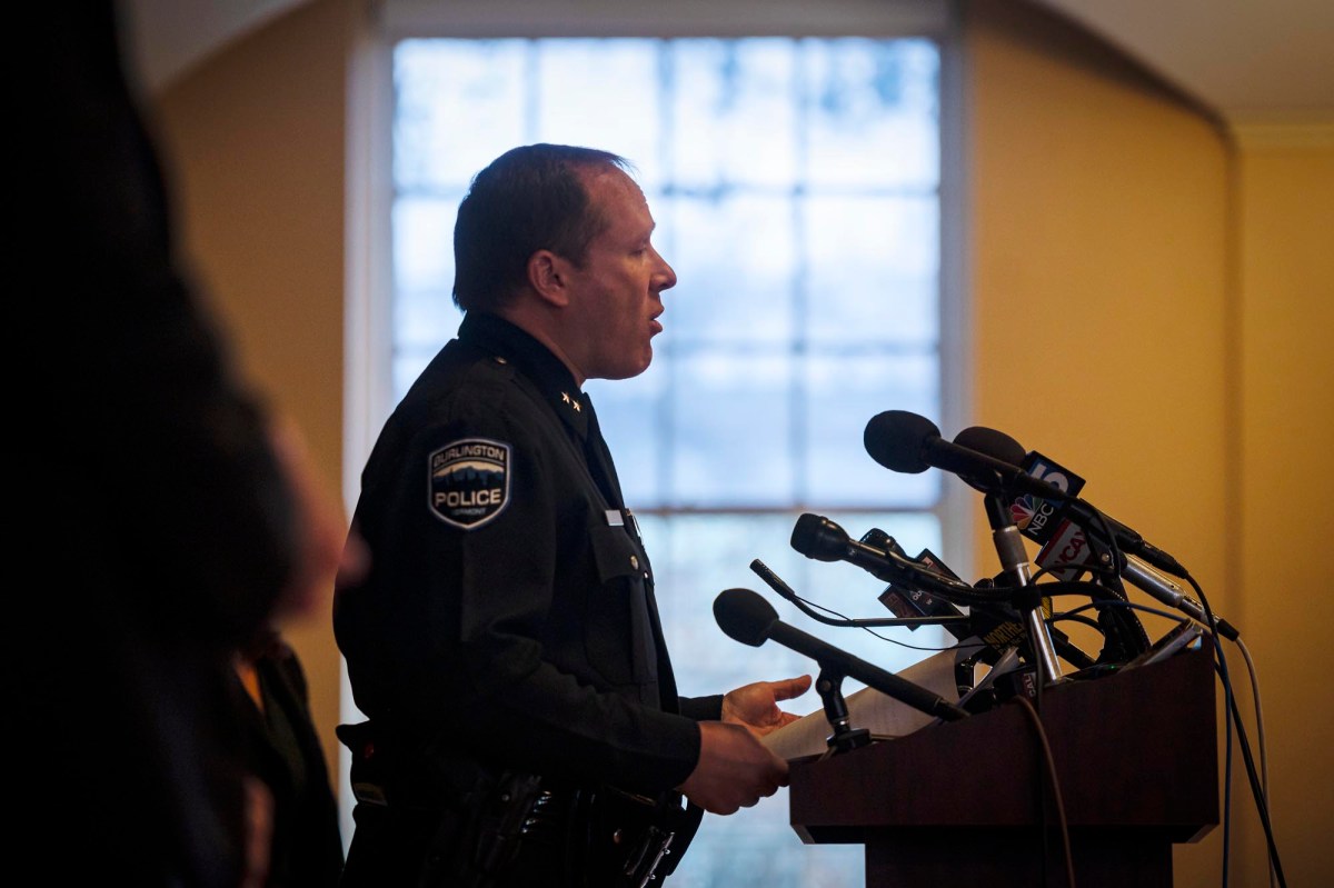 A police officer standing at a podium with microphones.