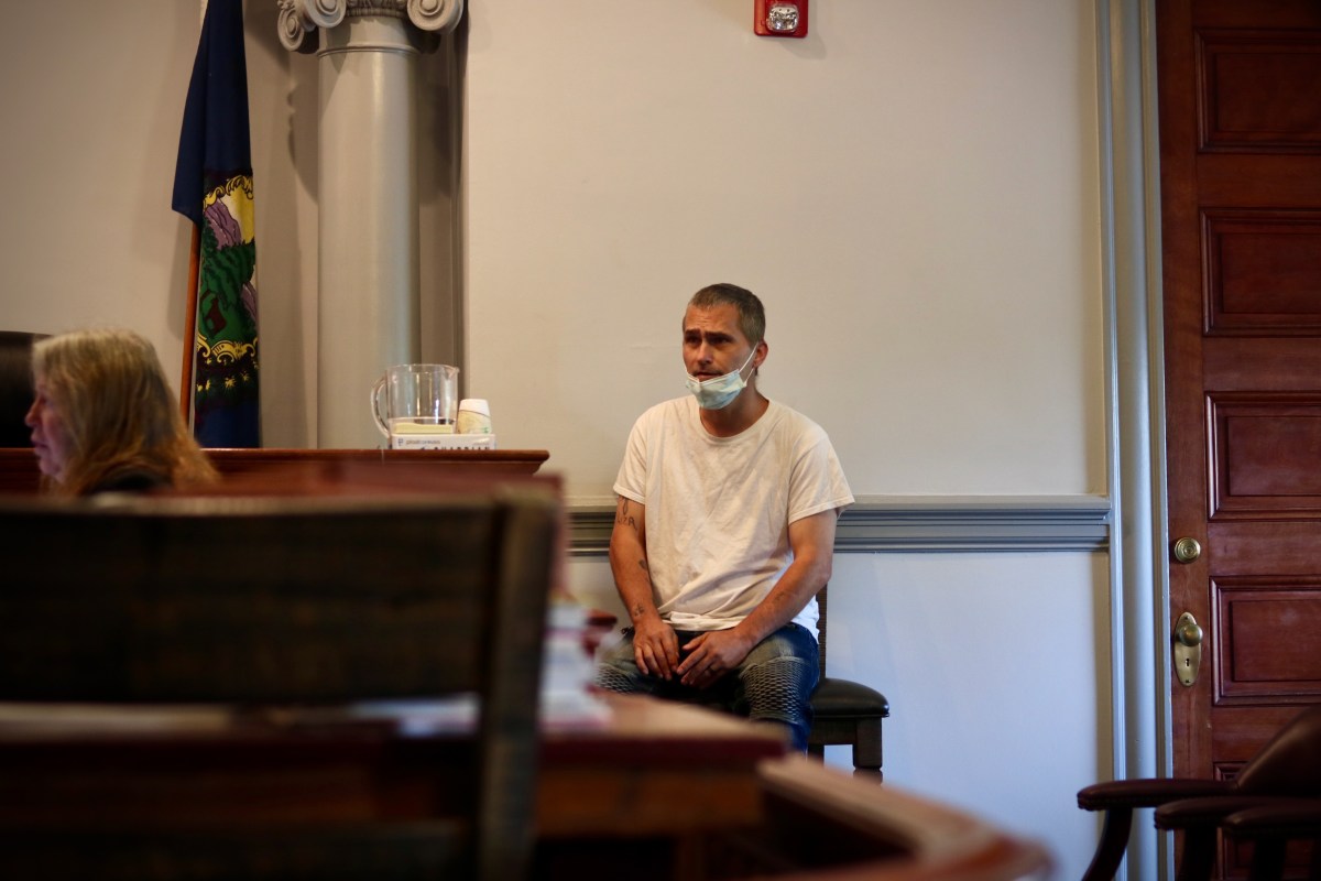 A man sitting in a courtroom with a face mask on.