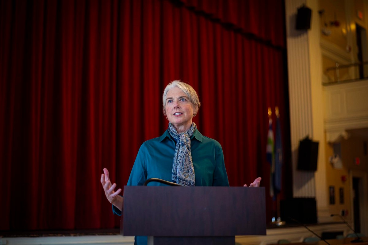 A woman standing at a podium in front of a red curtain.