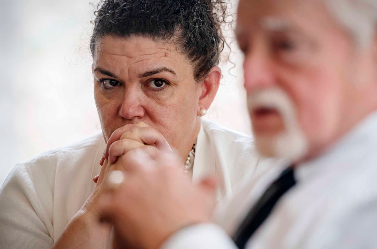Two professionals in a serious discussion; a middle-aged woman with curly hair and a man with white hair and beard, both appear focused and concerned.