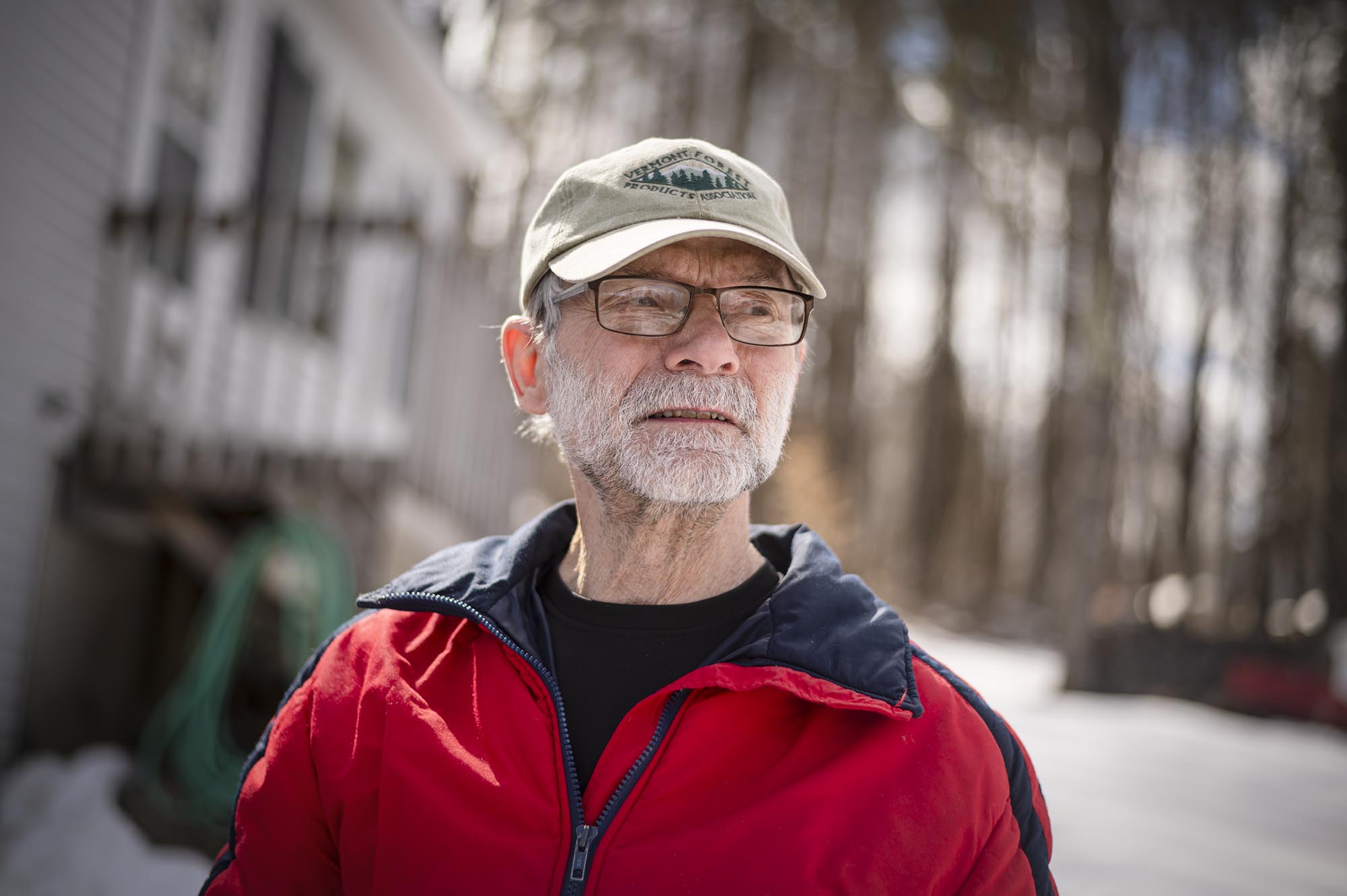 A man in a red jacket standing in front of a house.
