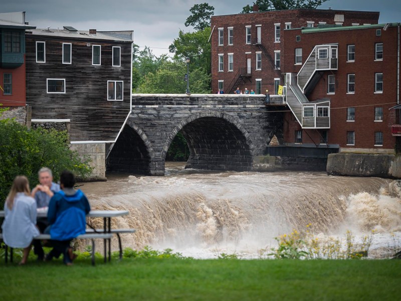 Two people sitting at a picnic table under a bridge.