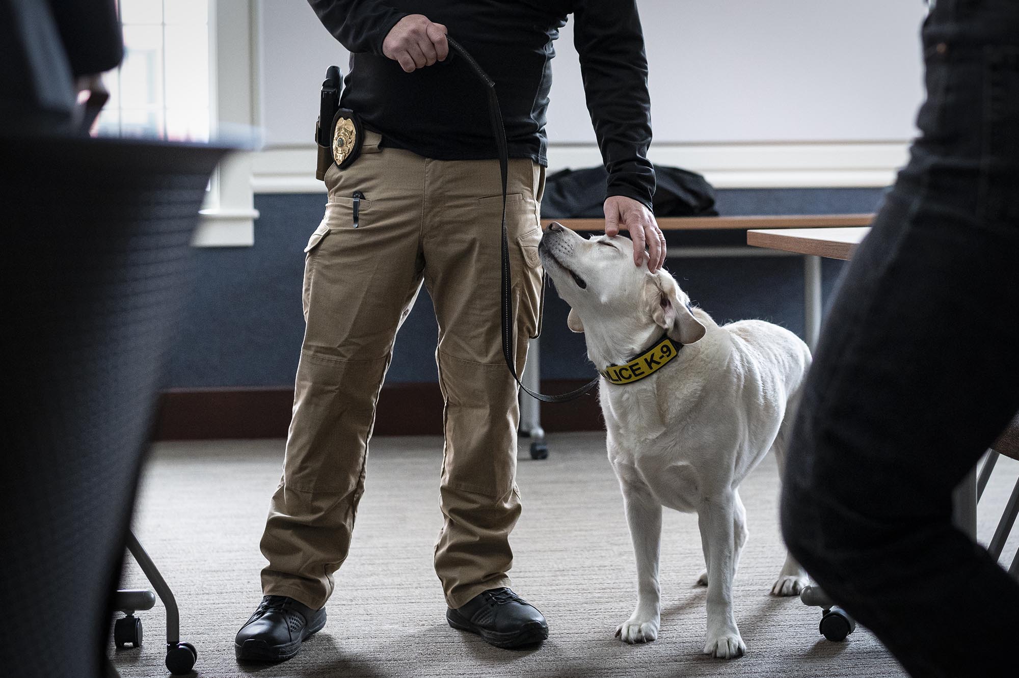 A police officer is petting a dog in a conference room.
