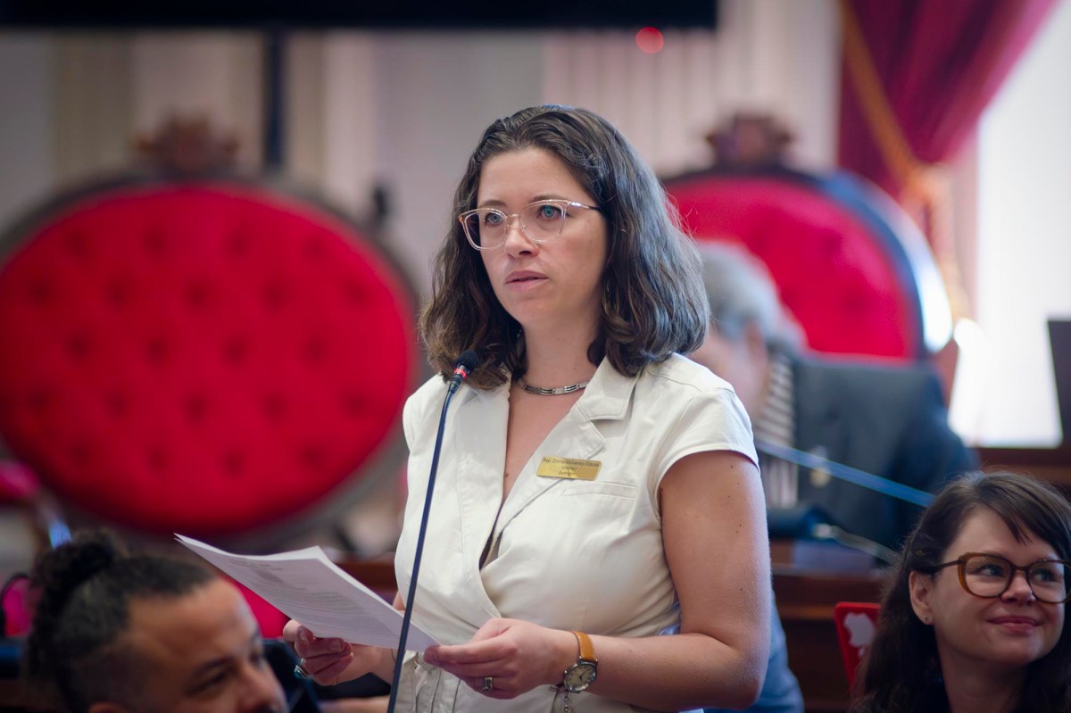 A woman in glasses is speaking into a microphone.