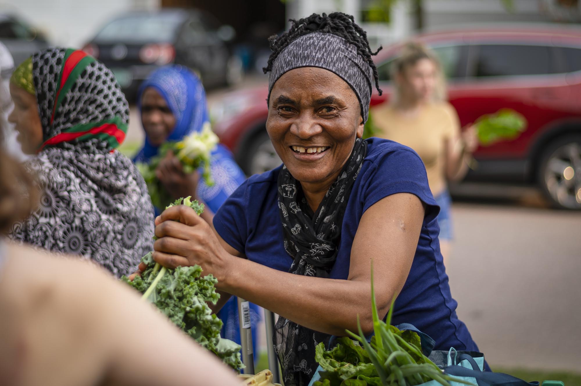 a woman smiles while holding a basket of vegetables.