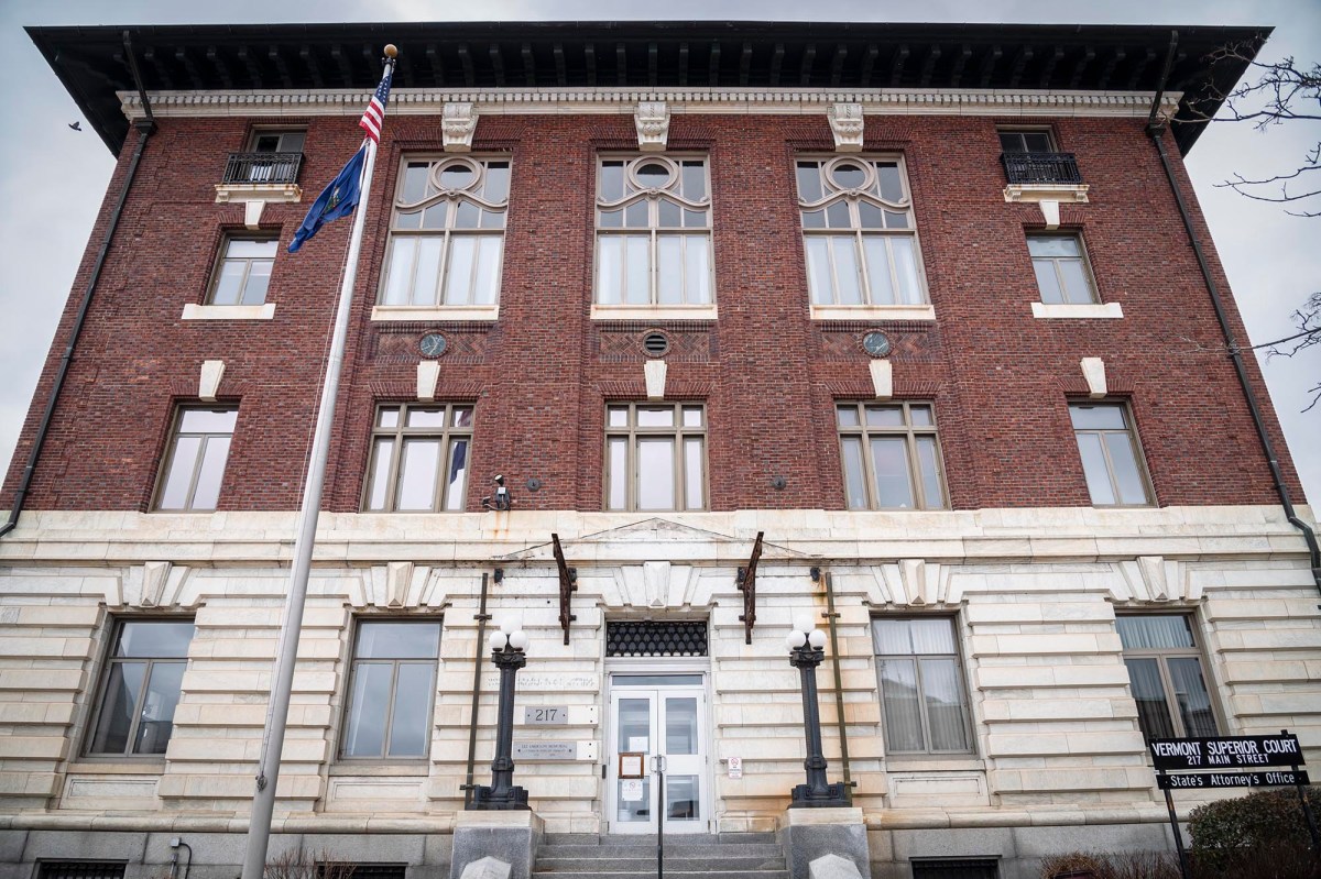 A brick building with stone foundations, featuring a central entrance flanked by lamps and flying american and state flags.