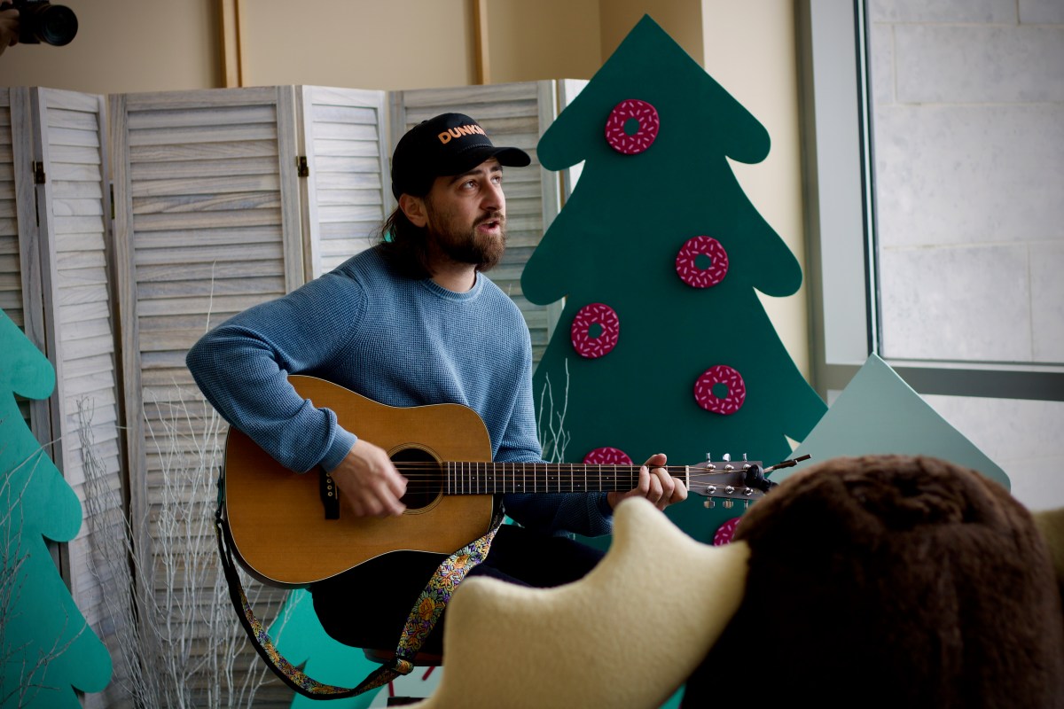 A man playing an acoustic guitar in front of a Christmas tree.