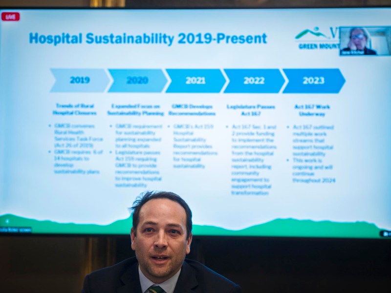 A man is standing in front of a tv screen with the words hospital sustainability 2019 present.