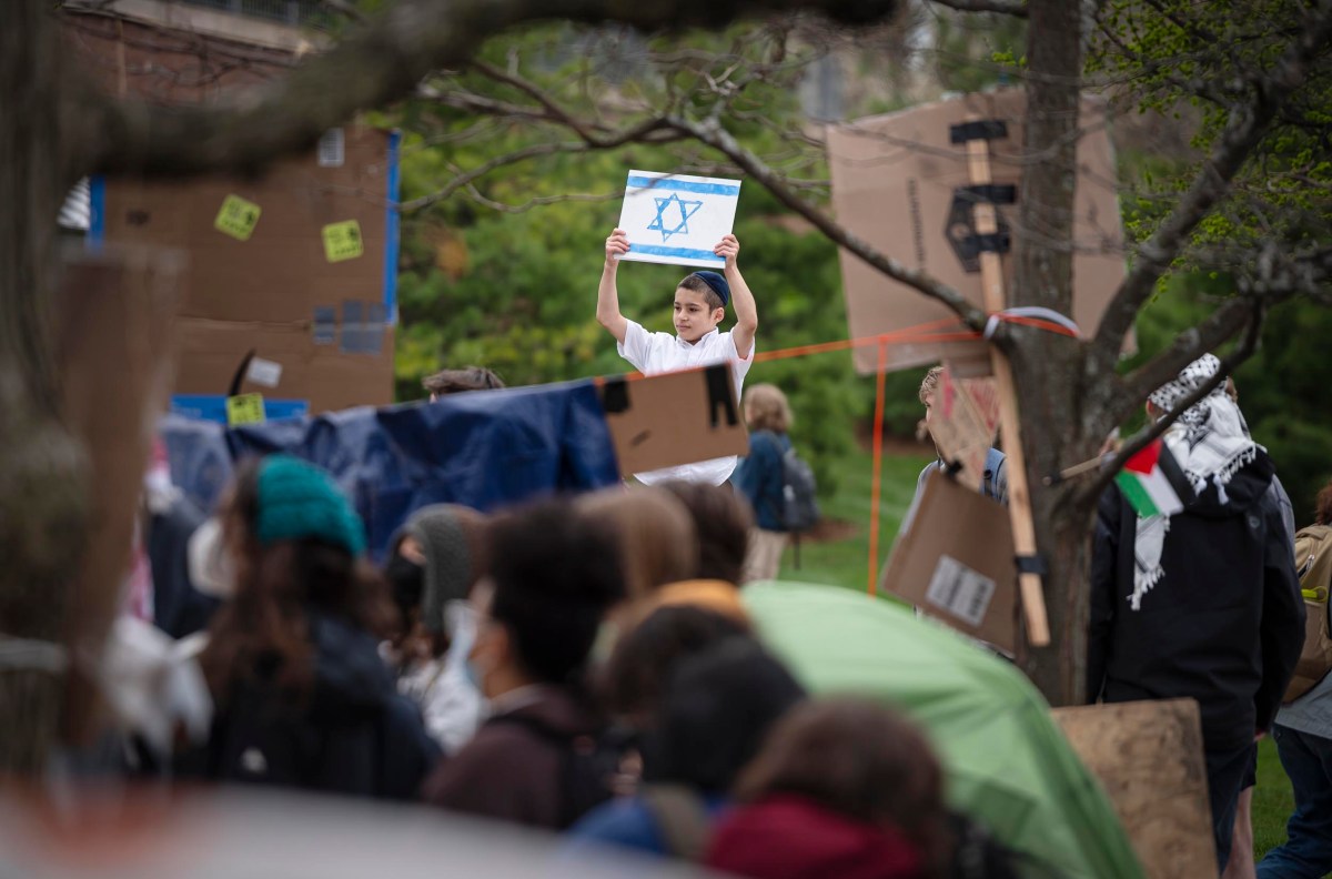 A person holding up a sign with a star of david in a crowd of demonstrators, surrounded by other signs and trees.