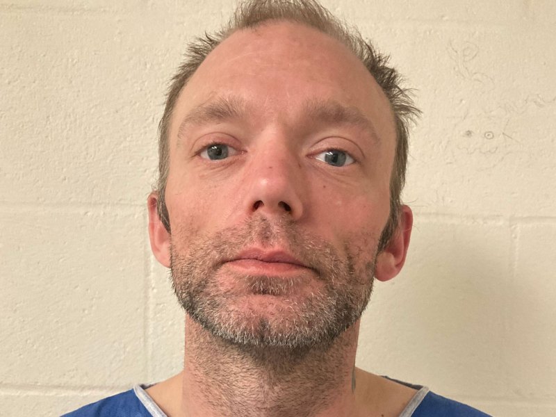A man standing against a cinderblock wall.
