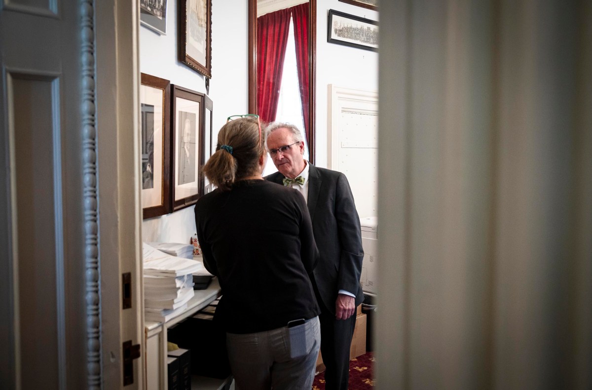 A man and a woman in a formal setting converse intently at the doorway of a well-lit office, surrounded by documents.