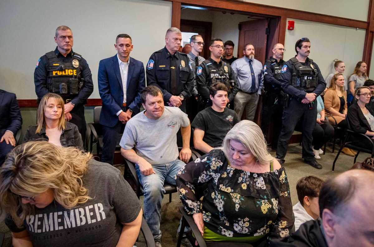 Uniformed police officers stand among seated civilians in a crowded room.