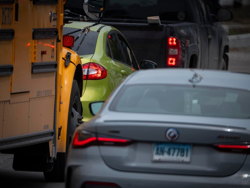 A yellow bus, a green car, and a silver car with Virginia license plates are in traffic.