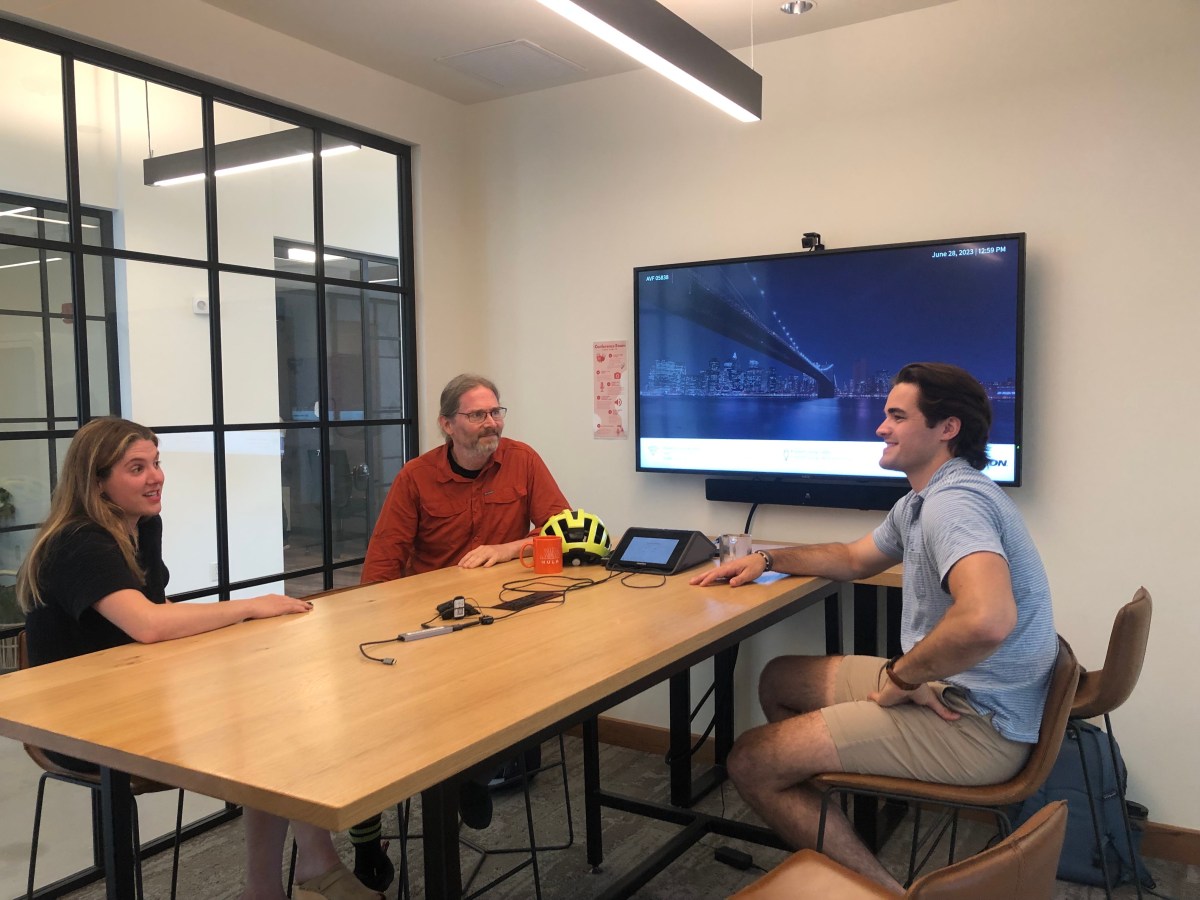 Three people sitting around a table with a tv in the background.