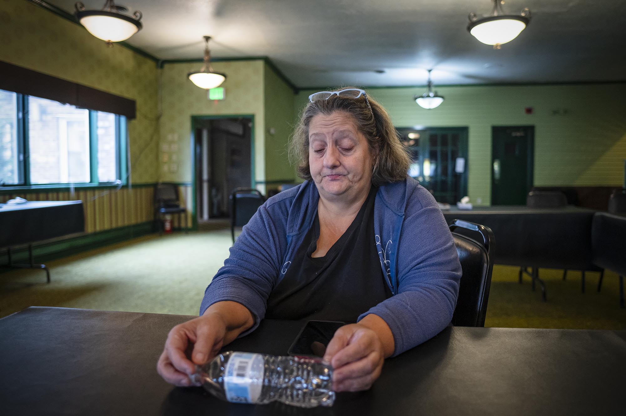 A woman sits at a table with a bottle of water.