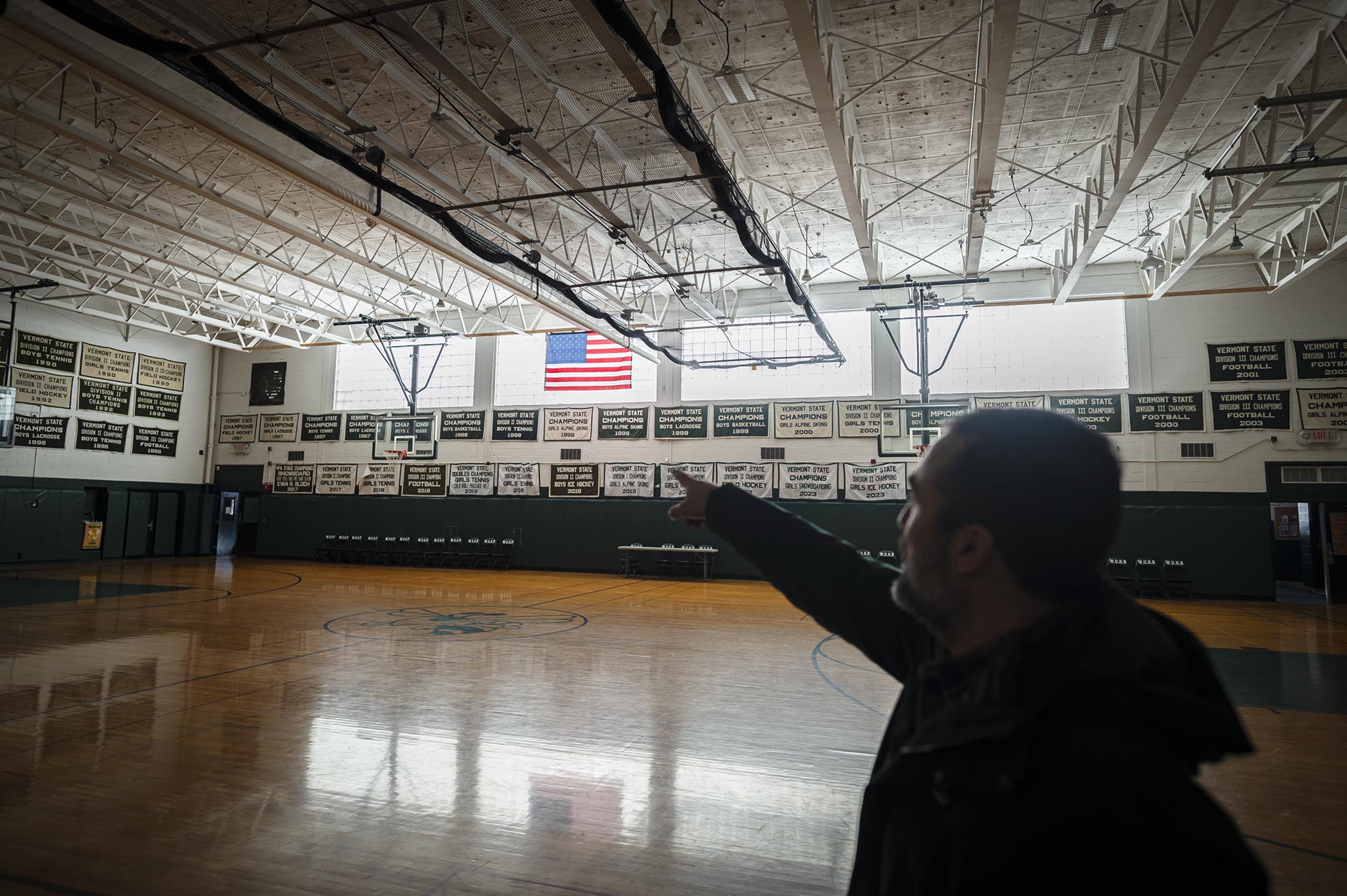 A man pointing at an american flag in a gymnasium.