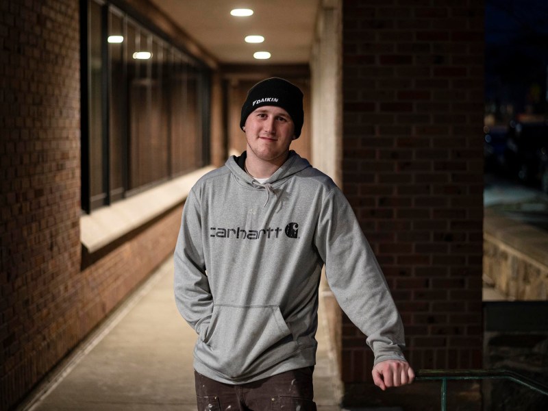 A young man in a gray hoodie standing in a hallway.