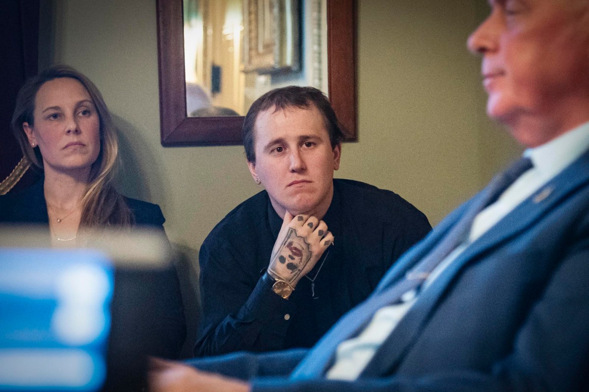 A man in a suit sits next to a man with tattoos.