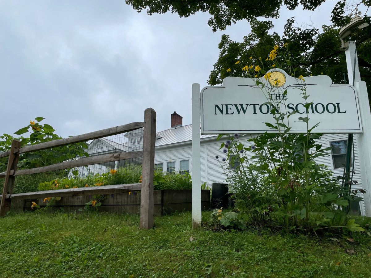 The sign for newton school is in front of a fence.