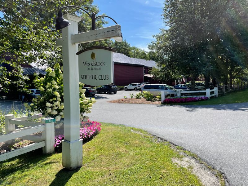 A white sign with flowers in front of it.